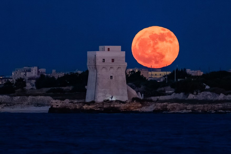 Flower Moon rises behind Torre Calderina with a dancer, in Molfetta, Italy.