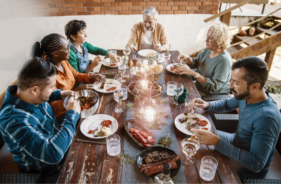 Six people, unidentified, enjoy a meal together at a wooden dining table with dishes and wine glasses. Candles in the center add warmth to the setting