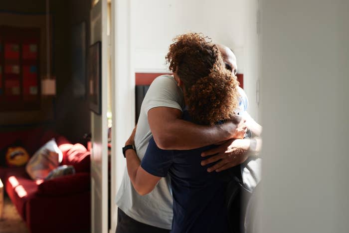 A man and a woman hugging each other warmly in a well-lit room with a red couch in the background