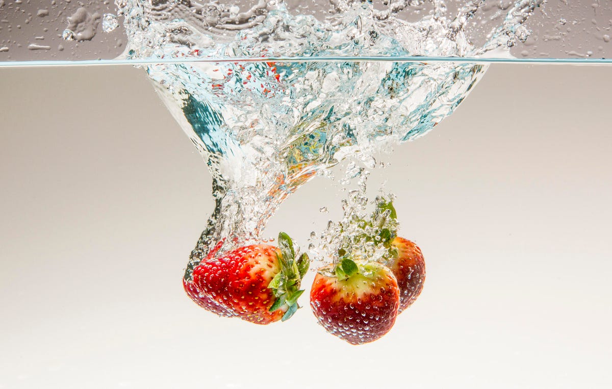 Three strawberries dunking into water.