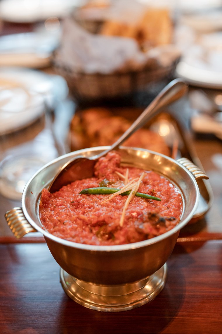 A dish of butter chicken is displayed on a dining table in a silver chalice