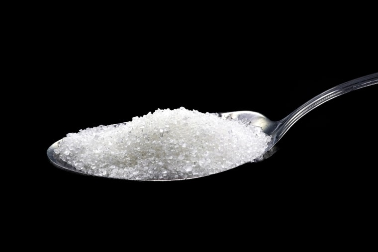 A small teaspoon with sugar, on a black background.