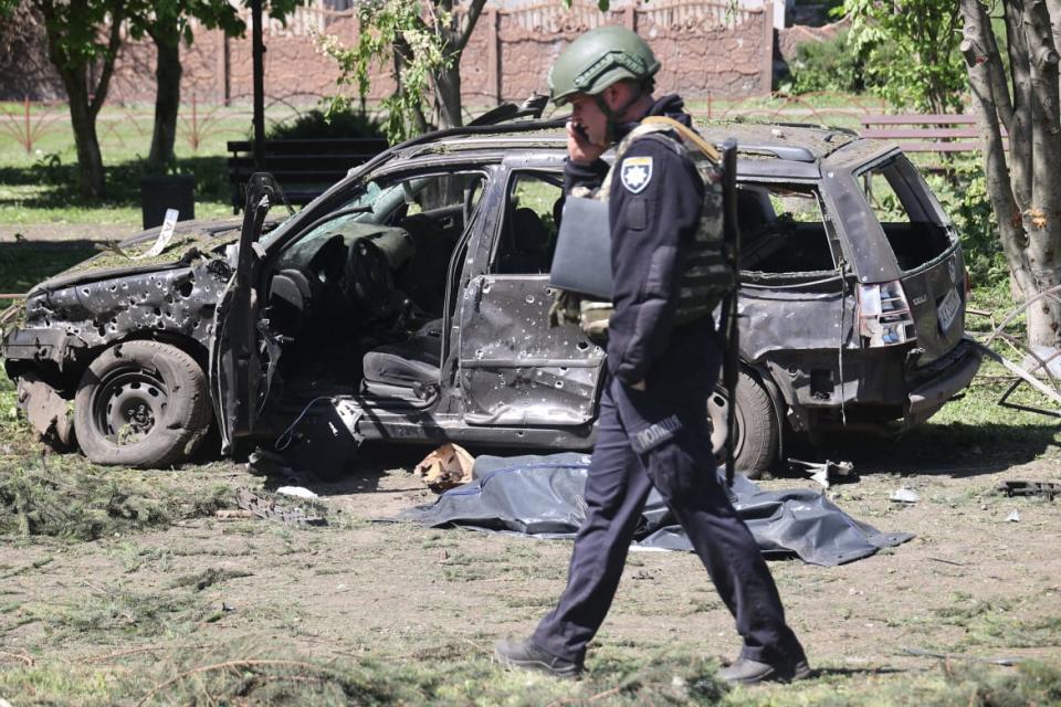 A Ukrainian police officer walks past a body bag near a damaged car in Zolochiv.