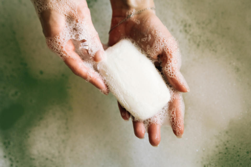 Close-up of two hands holding a bar of soap with lathered bubbles in a bath setting