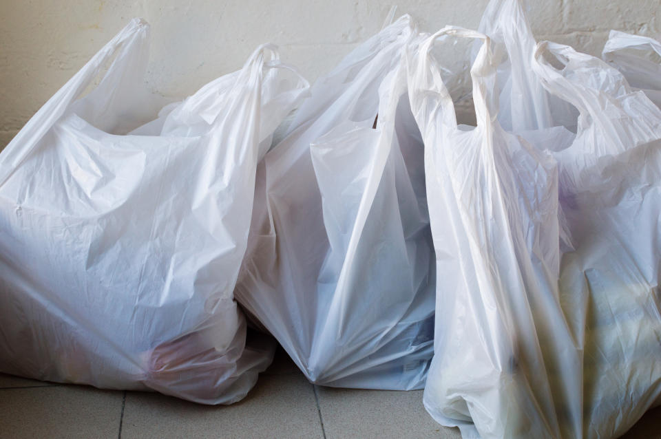 Plastic grocery bags filled with items are placed on a tiled floor
