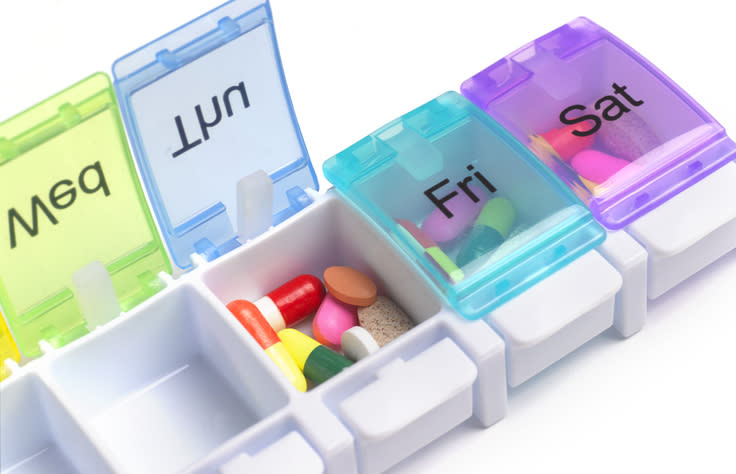 A weekly pill organizer with sections labeled "Sun," "Mon," "Fri," and "Sat," each containing various pills and tablets
