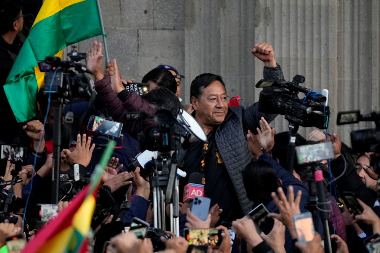 Bolivian President Luis Arce raises a clenched fist surrounded by supporters and media, outside the government palace in La Paz, Bolivia,
