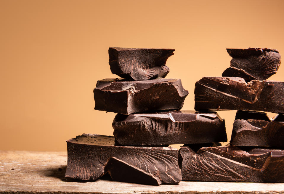 Chunks of dark chocolate stacked on a wooden surface against a plain background
