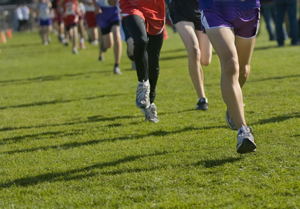 People running on a grassy field participating in a race. The focus is on their legs and footwear