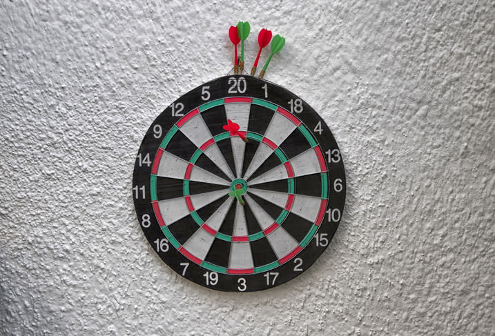 A dartboard with several darts, including one hitting the bullseye, is mounted on a wall