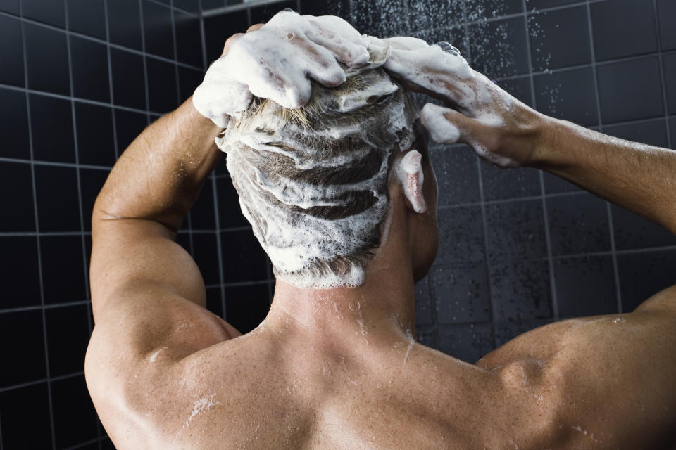 Person washing their hair in a shower, visible from the back with lathered hair and hands on their head