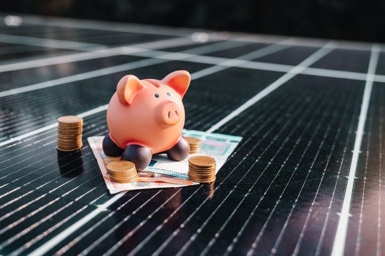 A piggy bank and money sitting on a solar panel.
