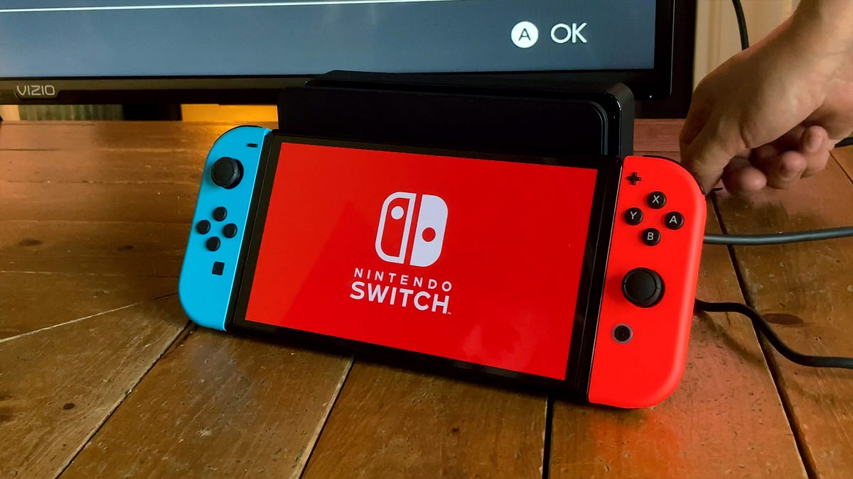a Nintendo Switch OLED with red and blue controllers sits next to a TV