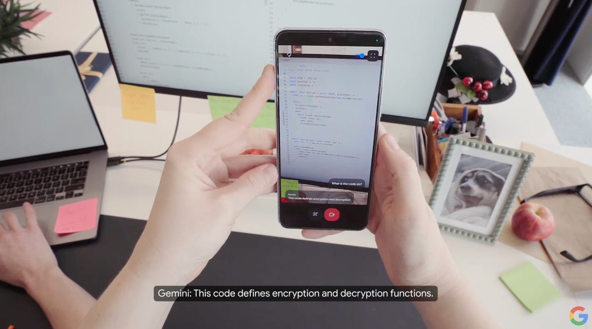 A phone looking at a computer monitor, interacting with an AI assistant with the camera