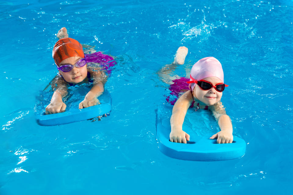 Two children with swim caps and goggles use kickboards while swimming in a pool