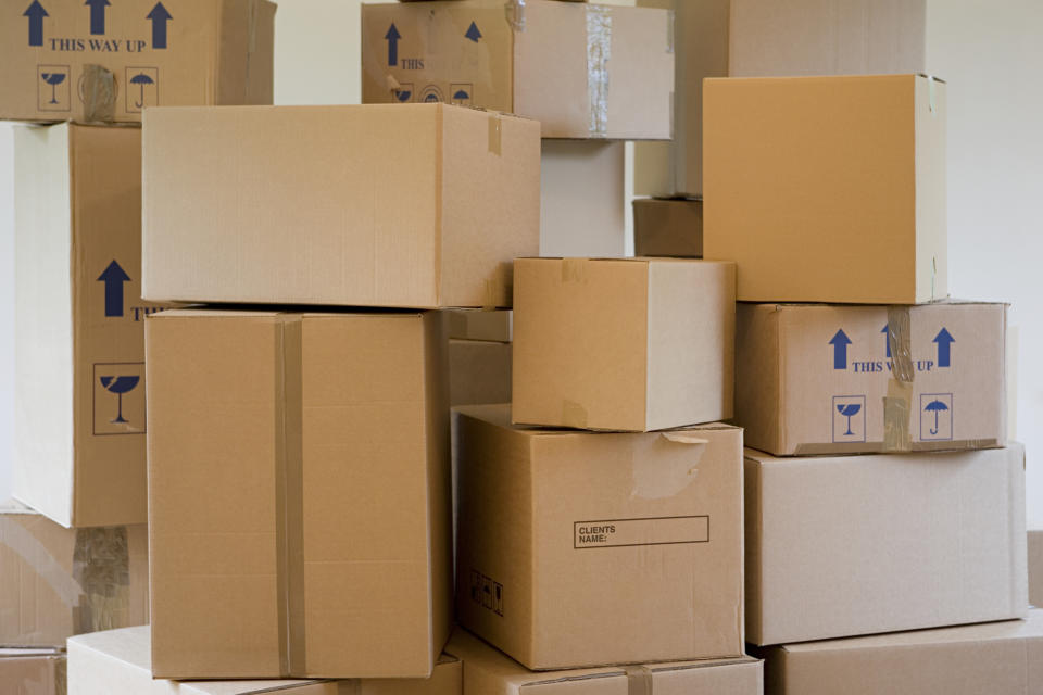 Stack of labeled and unlabeled moving boxes in various sizes, some with "This Way Up" and fragile item symbols, indicating a packing or moving scene