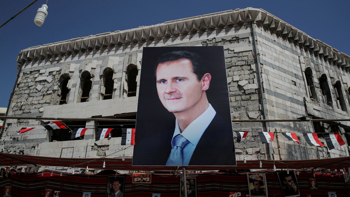 FILE PHOTO: A man walks past a banner depicting Syrian president Bashar al-Assad in Douma, outside Damascus, Syria, September 17, 2018.