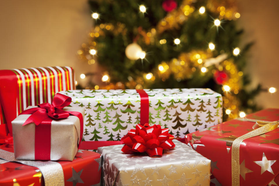 Christmas presents wrapped in festive paper with bows are arranged under a decorated Christmas tree with lights