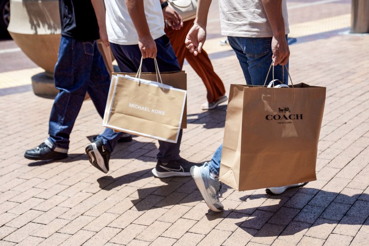 People hold Coach and Michael Kors shopping bags while walking outside