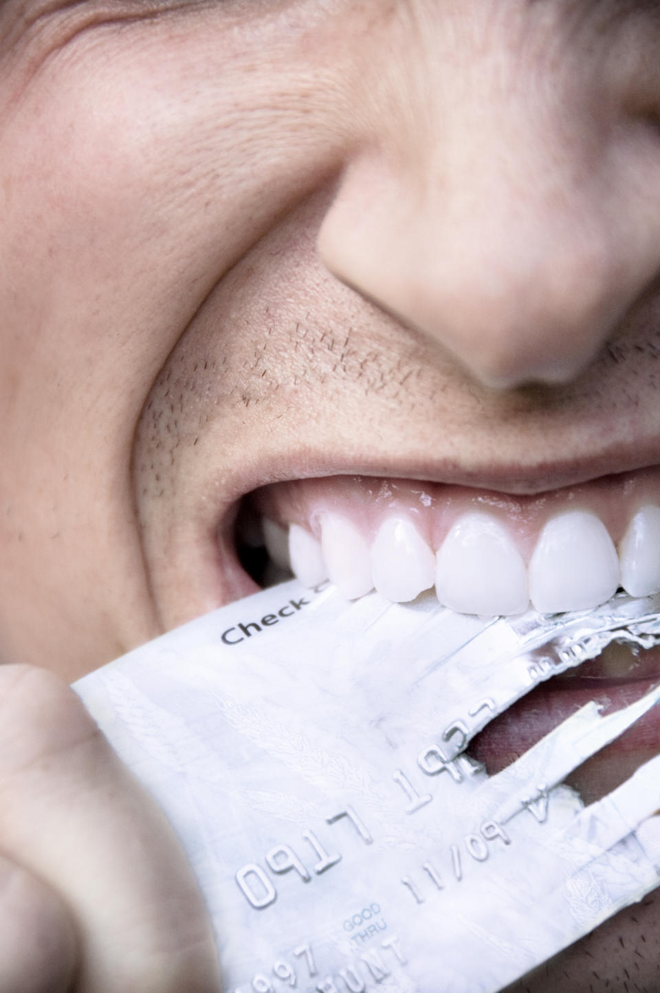 A person is biting into a credit card with visible clenched teeth, partially shredding the card. No additional context or text is provided