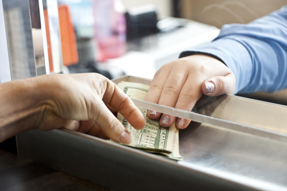 A person hands money to another person through a bank teller window
