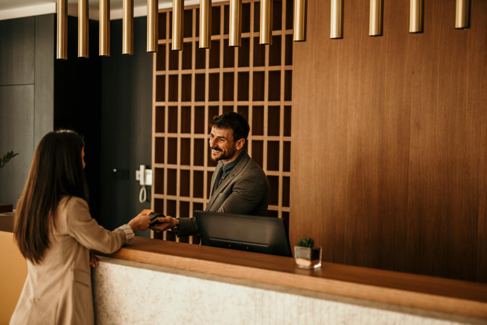 A businessperson is smiling while handing a card to a receptionist at a modern hotel front desk