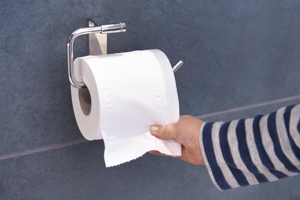 A person wearing a striped sleeve is pulling a sheet from a wall-mounted toilet paper roll in a bathroom setting