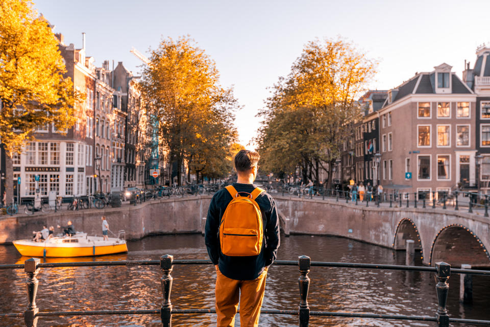 Person with a backpack stands on a bridge overlooking a canal and historic buildings in a city, likely reflecting on work and travel