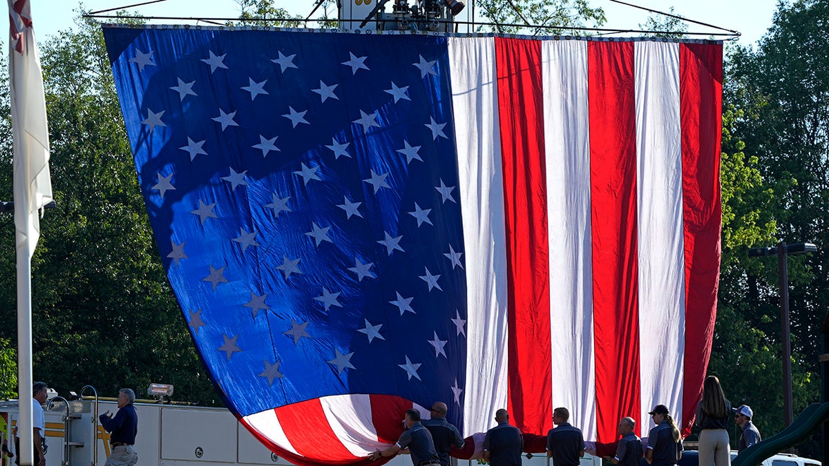 A giant American flag is unfurled outside the Cabot Church before the funeral service for Buffalo Township Volunteer fireman Corey Comeratore