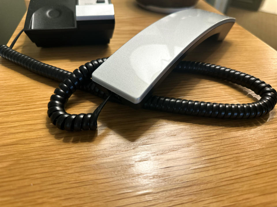 A close-up of a desk phone's handset resting on its coiled cord atop a wooden surface