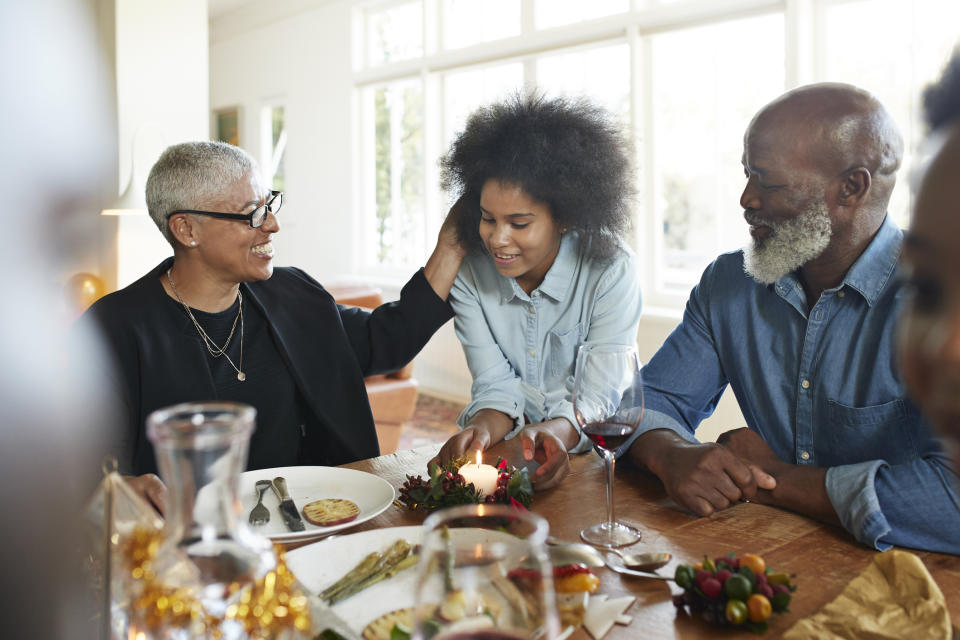 An elderly woman, young girl, and elderly man share a meal at a warmly lit table, smiling and interacting with each other