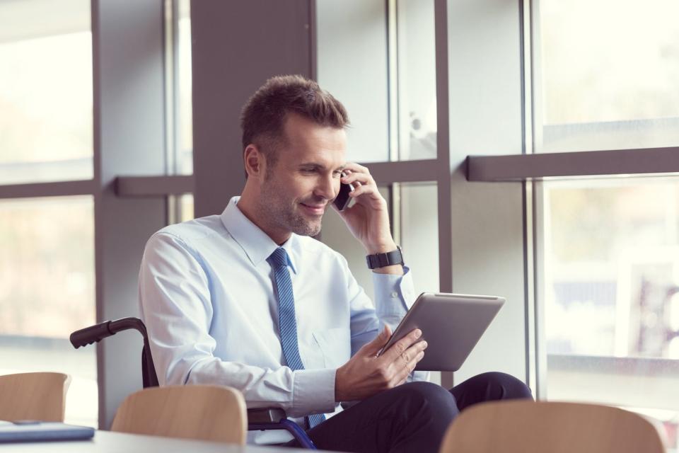 An investor in an office looks at a tablet and talks on the phone.