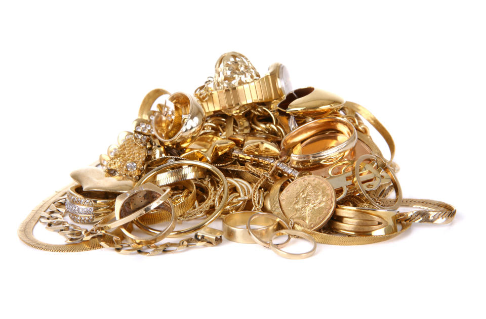 A pile of various gold jewelry, including rings, bracelets, necklaces, watches, and other accessories, set against a plain background