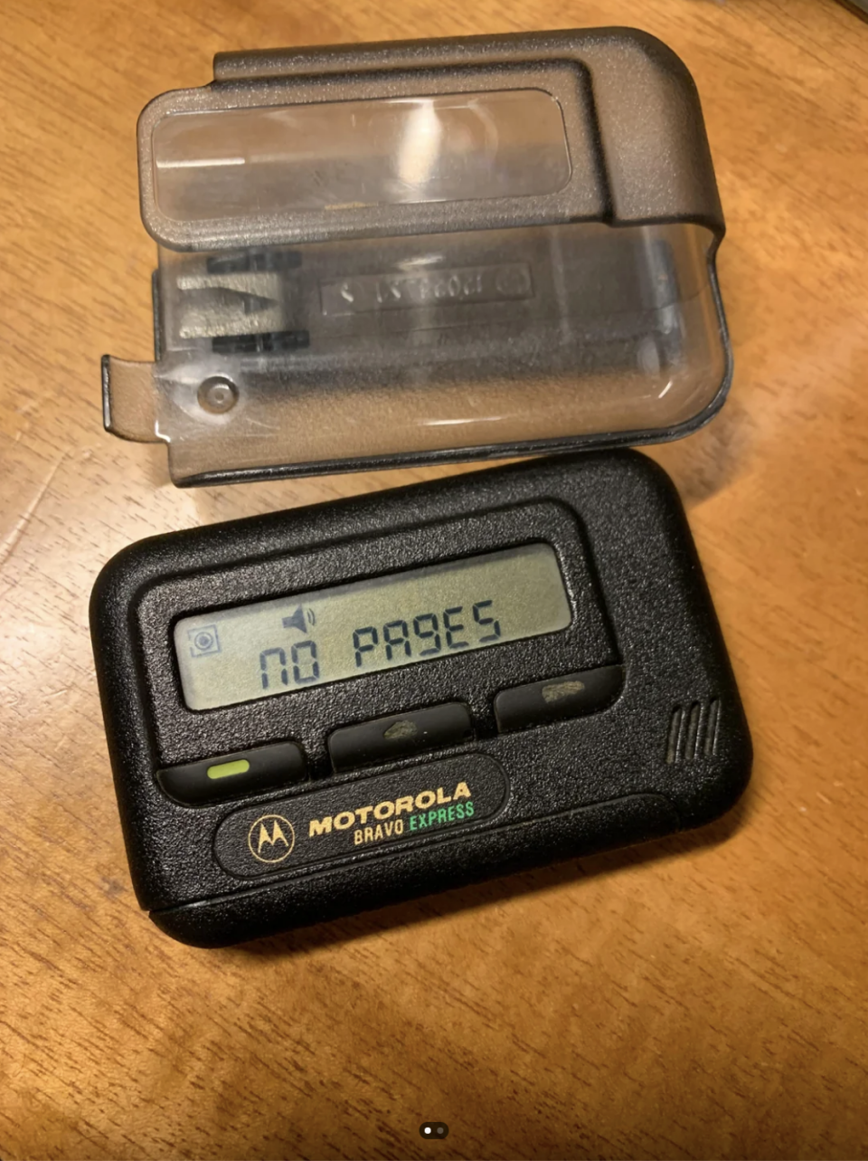 Motorola Bravo Express pager, displaying "NO PAGES" on screen, with its clip cover placed beside it on a wooden surface