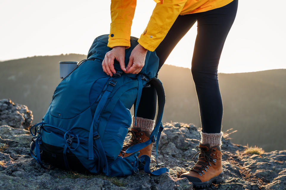 A person in outdoor gear, including hiking boots and a backpack, prepares for a hike on a rocky terrain at sunset
