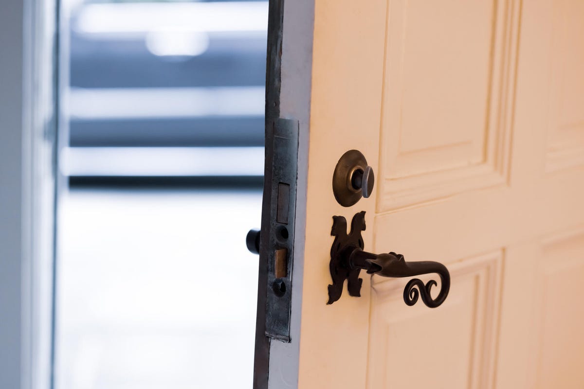 A brown house door with ornate black handle left open.