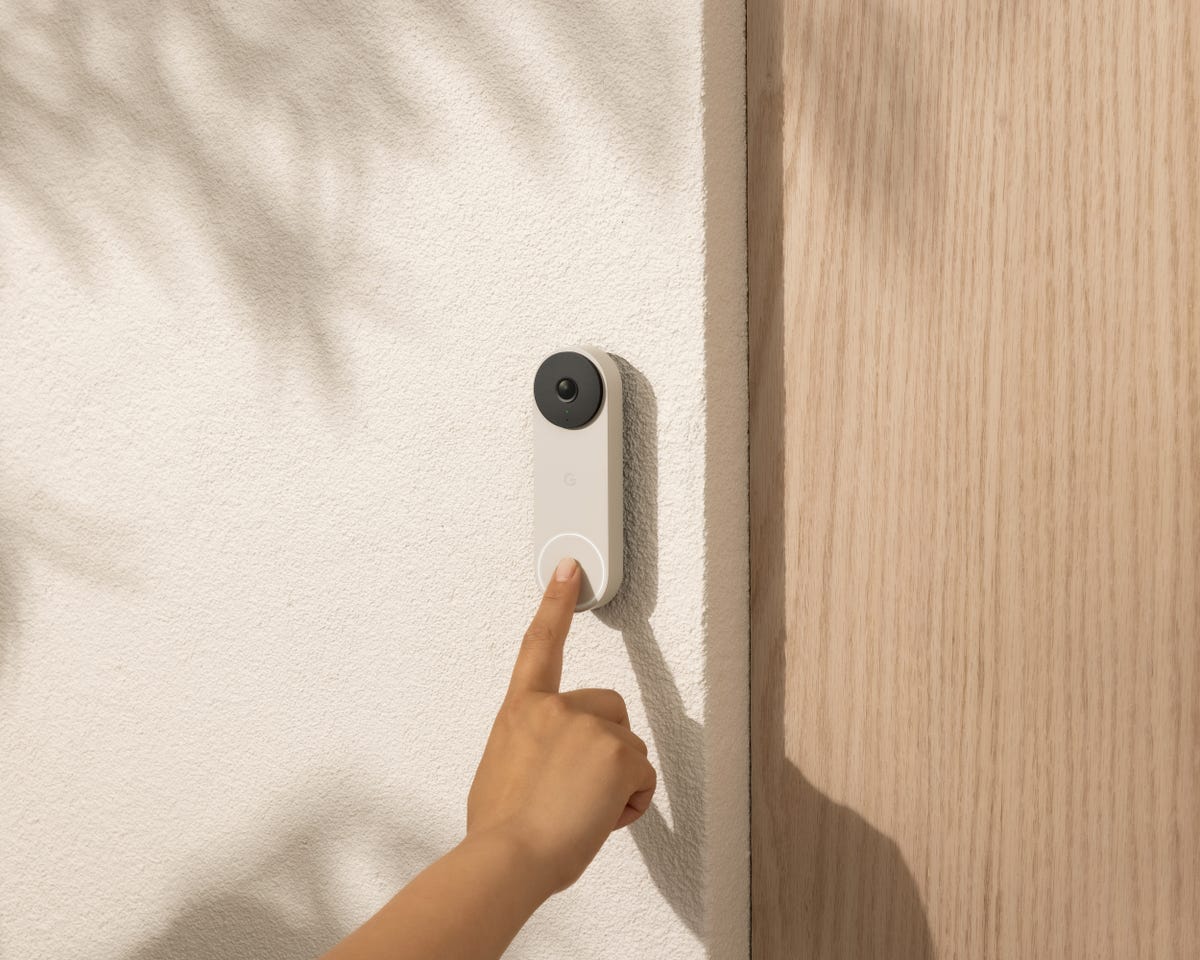 A child's hand reaches up to ring the hardwired Nest Doorbell at a sunlit front door.