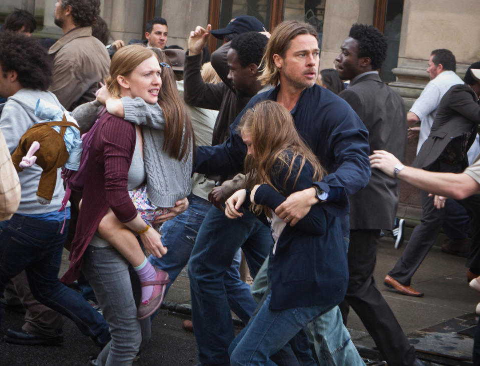 Brad Pitt and Mireille Enos in a crowded scene from "World War Z." Brad is holding a young girl while guiding a woman, suggesting urgency and protection