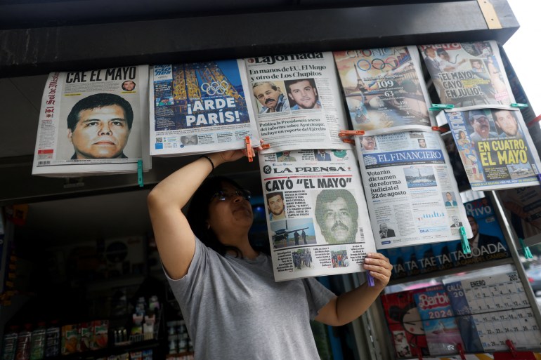 A newspaper salesperson arranges broadsheets showing the arrest of El Mayo on the cover.