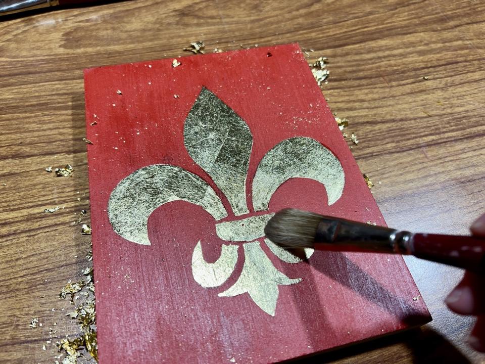 A brush brushes away gold leaf from a painting in Florence.