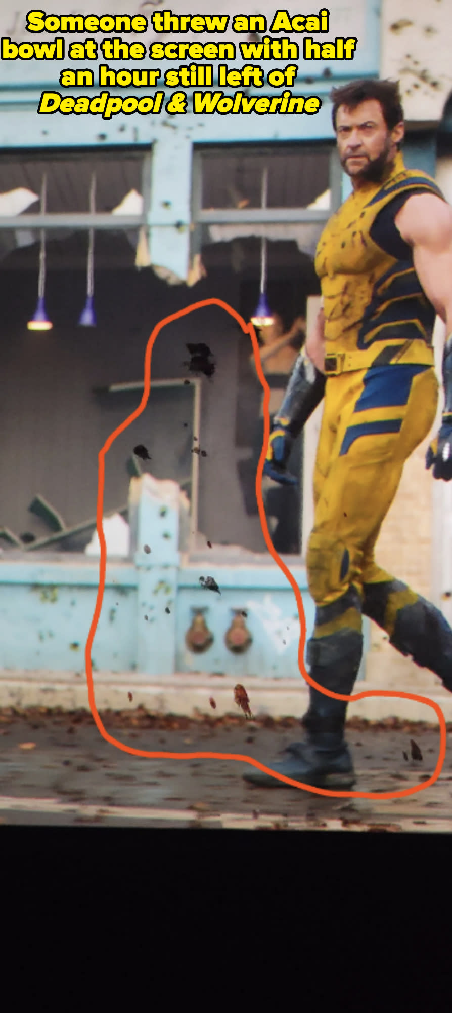 Hugh Jackman dressed as Wolverine, wearing a yellow and black costume with gloves, walking in front of a damaged building