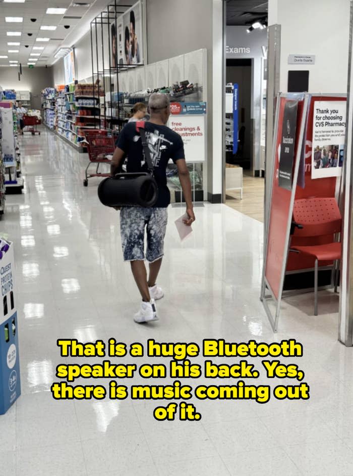 A man with a cylindrical object walks through a store aisle filled with various products on shelves