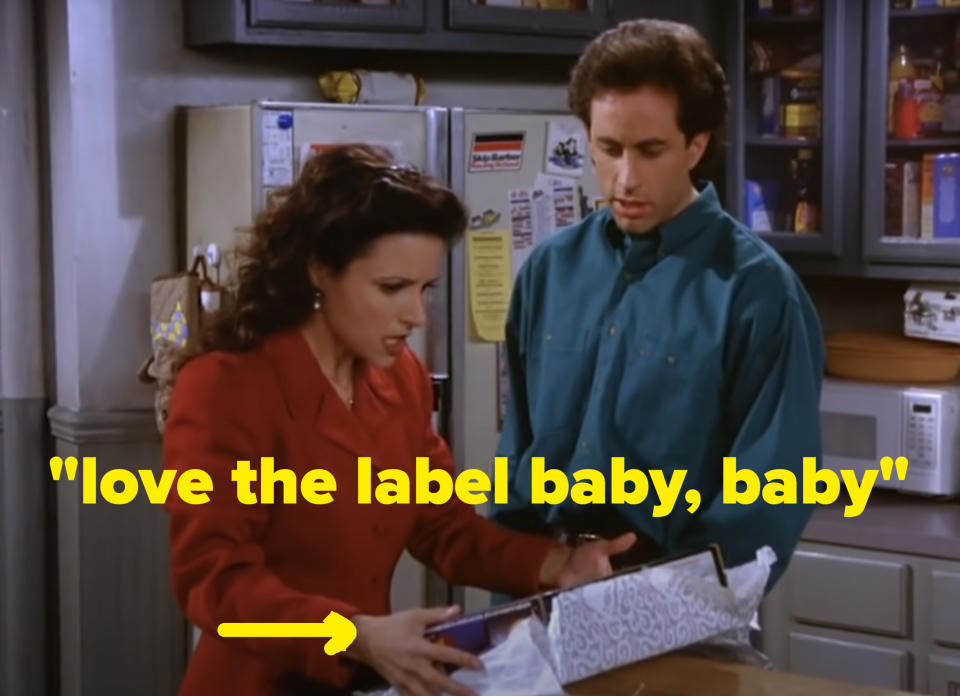 Elaine from "Seinfeld" is opening a gift box with a surprised expression while Jerry looks on