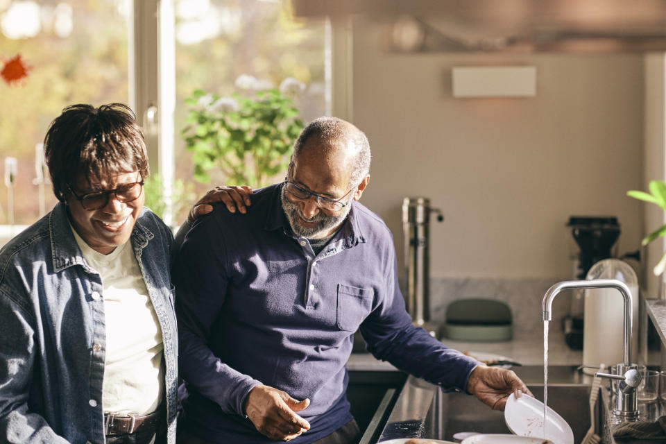 An older couple enjoys their time together, smiling and washing dishes in a cozy kitchen with sunlight coming through the window