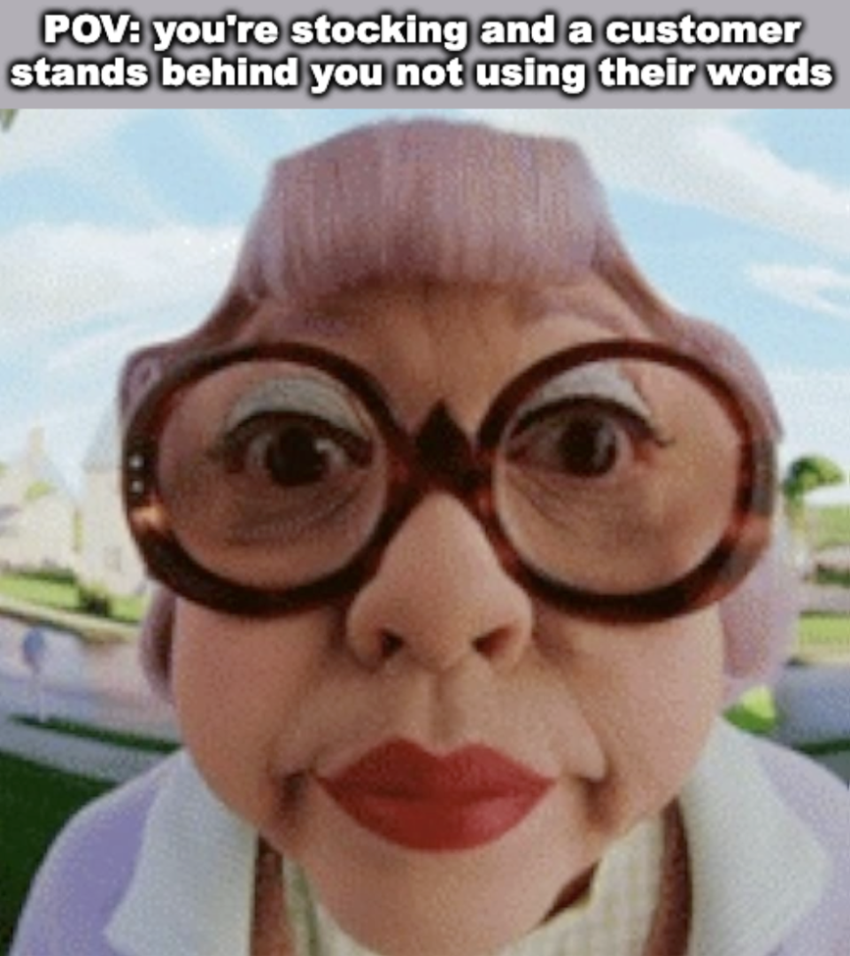 Close-up of a cartoonish elderly woman with large glasses and pursed lips, captioned "POV: you're stocking and a customer stands behind you not using their words."