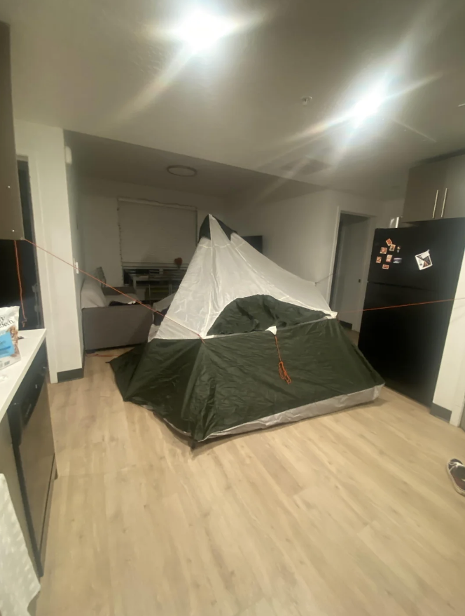 A large camping tent is set up in the middle of a modern kitchen, with counters and appliances surrounding it