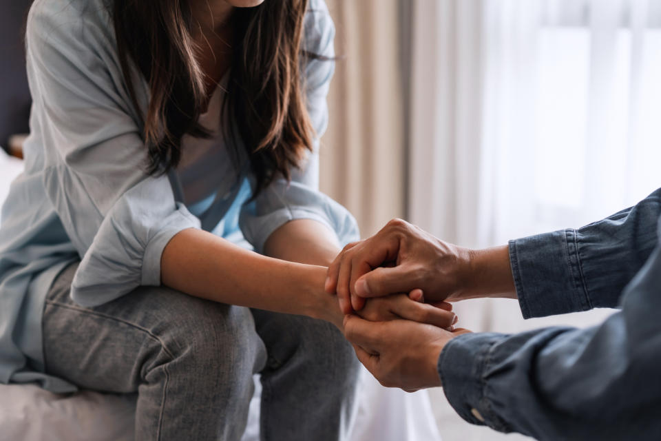 A woman and a man are sitting, holding hands in a comforting manner