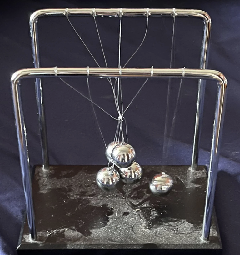 A Newton's cradle with five metallic balls is shown, with one ball elevated ready to be released