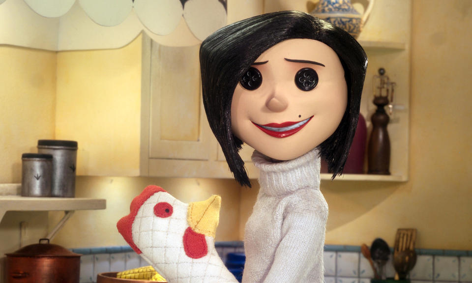 Coraline's Mother in a kitchen scene holding a chicken-shaped oven mitt. She has button eyes, a bob haircut, and is wearing a turtleneck sweater