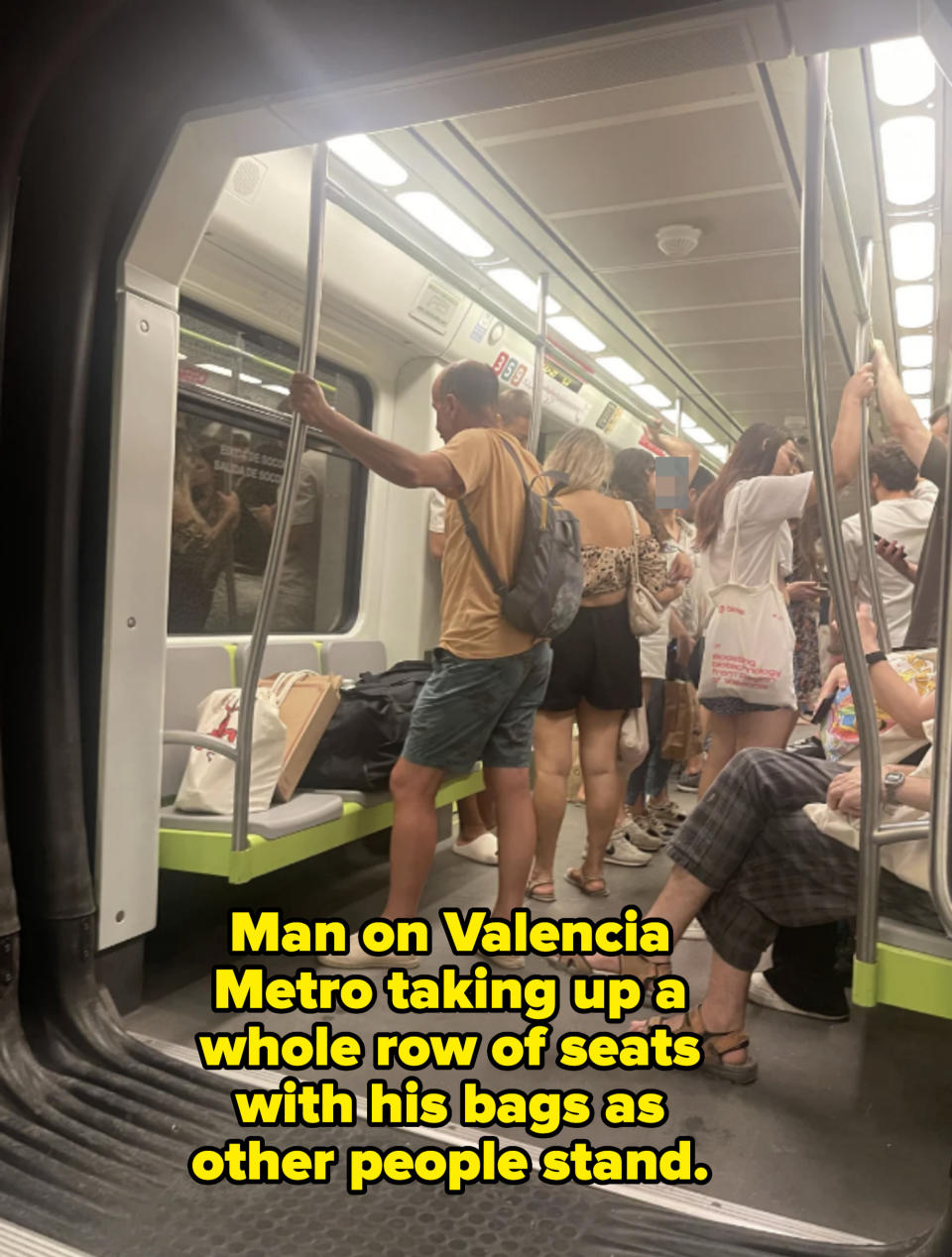 People standing and sitting inside a subway train, with various passengers holding onto poles and carrying bags